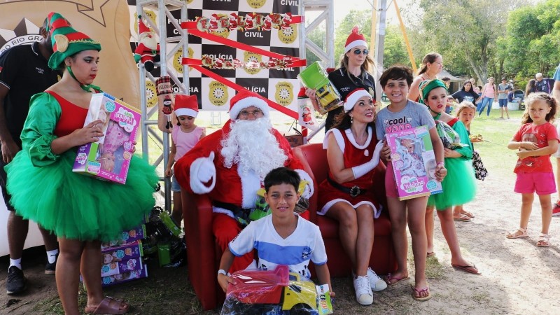 Foto mostra crianças com brinquedos ao lado do Papai Noel. 