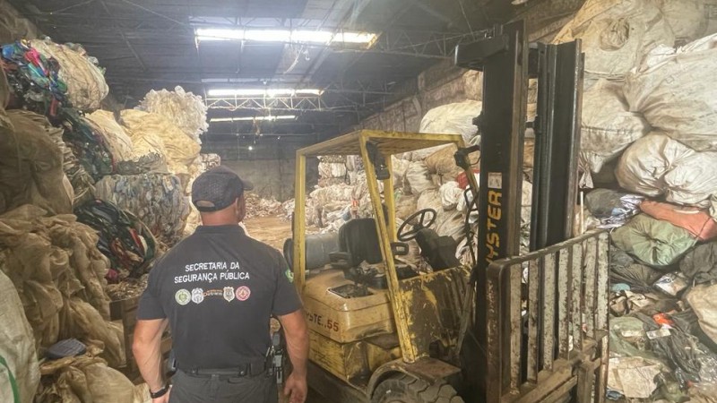 Foto mostra homem de costas. Ele veste camiseta da SSP e olha para galpão cheio de sucata em empresa de reciclagem.