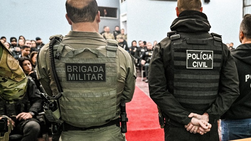 Um policial civil e um brigadiano, de costas, falando com um publico de policiais sentados em um auditório