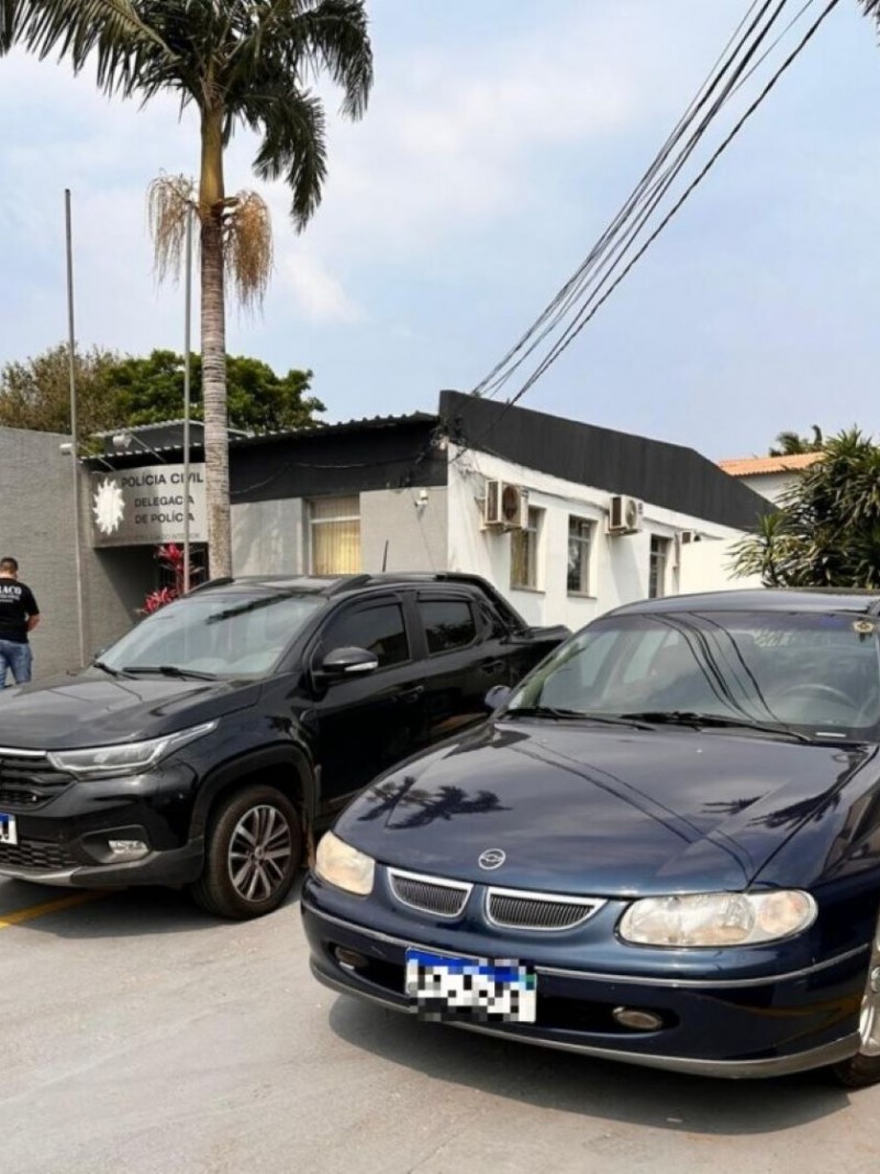 A foto mostra dois carros em frente a delegacia de polícia