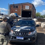 A foto mostra dois policiais militares e uma viatura da Polícia Civil em frente a um ponto de reciclagem