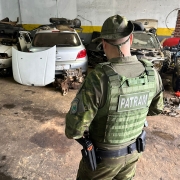 A foto mostra um policial militar vistoriando um desmanche automotivo