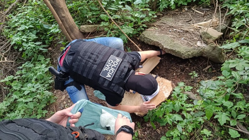 A foto mostra um policial fazendo buscas de drogas em baixo de uma pedra