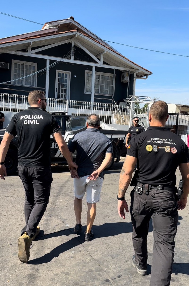 Homem detido sendo conduzido por dois agentes de segurança