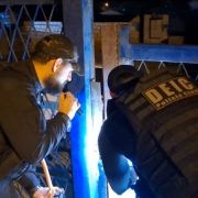 A imagem mostra dois agentes cumprindo mandato de busca e apreensão durante a operação policial