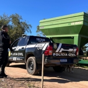 Agente da Polícia Civil em pé, diante da camionete da corporação, em frente ao graneleiro de cor verde apreendido na operação. 