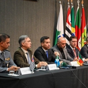 Na mesa de abertura do evento há seis pessoas, com as miniaturas das bandeiras dos estados de cada um à frente. Ao fundo, as bandeiras em posição de cerimonial.