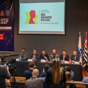 Os seis representantes das Secretarias de Segurança Pública estão sentados em uma mesa no palco do auditório. À frente, repórteres durante a coletiva de imprensa. Ao fundo, projetada, a logo do Governo do Estado do Rio Grande do Sul e o banner do evento, onde se lê "SULMaSSP Em Porto Alegre | RS" e "Encontro estratégico de Segurança Pública".