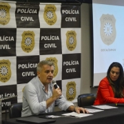 No palco do evento, especialista fala ao microfone ao lado de outra palestrante. Atrás deles, banner da Polícia Civil e uma tela de projeção onde se lê "Summit Crimes Digitais contra crianças e adolescentes" ao lado do escudo da Polícia Civil.