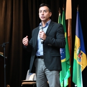 Sandro Caron na abertura do 3º Congresso Internacional de PJM, no palco. Atrás, bandeiras perfiladas.