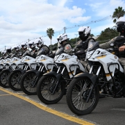 Novo motos brancas estão enfileiradas, todas montadas por brigadianos com capacetes brancos.