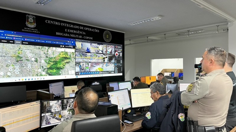 A imagem mostra policiais e agentes de segurança observando mapas e câmeras de monitoramento no Centro Integrado de Operações e Emergência