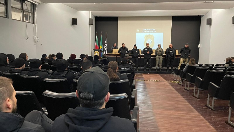 Integrantes da Polícia Civil e da Brigada Militar no auditório do Palácio da Polícia. Seis pessoas estão à frente, uma delas falando para plateia, onde há várias pessoas sentadas com uniformes das corporações.