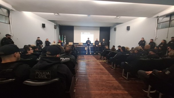A imagem mostra um auditório com agentes uniformizados