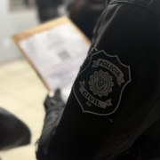 A imagem mostra parcialmente um agente da Polícia Civil uniformizado que segura envelope e se prepara para a operação O Infiltrado