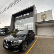 Um automóvel preto de luxo apreendido está estacionado na frente da delegacia de Polícia de Caxias do Sul.