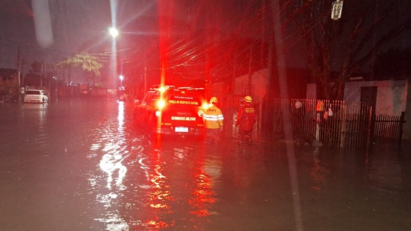 A imagem mostra uma viatura do Corpo de Bombeiros Militar em uma rua alagada. Na imagem, há dois agentes do CBM, que estão ajudando nos resgates