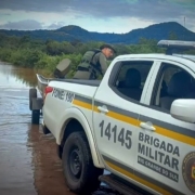 A imagem mostra uma viatura da Brigada Militar em uma região alagada do Estado. Há também dois agentes da Brigada Militar que estão participando dos resgates 