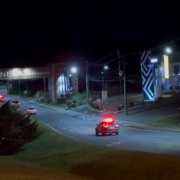 A imagem mostra viaturas da Polícia Civil cruzando o pórtico de entrada da cidade de Canela 