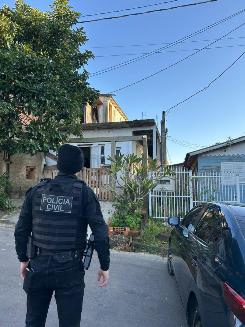 Policial ao lado de automóvel se prepara para entrar em residência