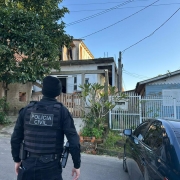 Policial ao lado de automóvel se prepara para entrar em residência