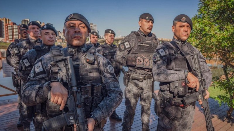 A imagem mostra um grupo de policiais do batalhão de operações especiais. Todos estão fardados com o uniforme do batalhão e usando boinas da cor preta. Os dois primeiros da foto empunham fuzis, enquanto os demais estão em posição de descanso