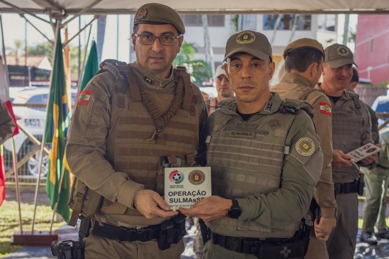 A imagem mostra um policial militar do Estado de Santa Catarina, à esquerda, e o subcomandante-geral da Brigada Militar, coronel Douglas da Rosa Soares, à direita. Ambos seguram uma placa que celebra a Operação SULMaSSP