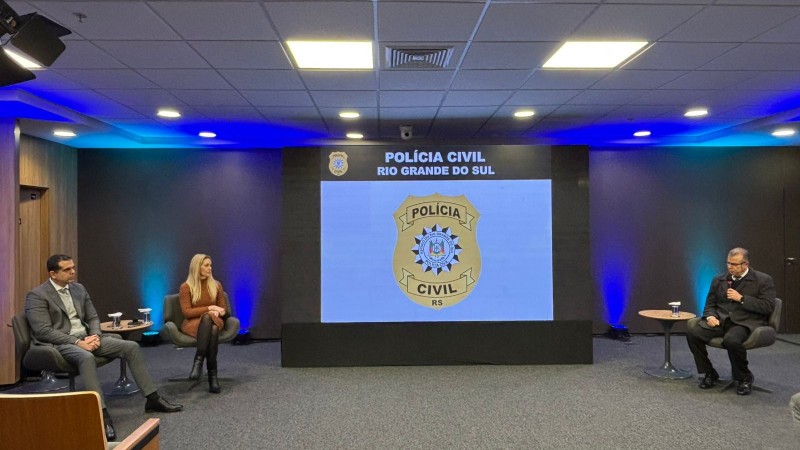 Painel teve palestras da subchefe Adriana Costa e do delegado Wendt (Denarc), sentados à esquerda do palco, com mediação do des. Marco Xavier (TJRS), sentado à esquerda, com o microfone,. Ao centro, telão com a logo da PC.