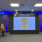Painel teve palestras da subchefe Adriana Costa e do delegado Wendt (Denarc), sentados à esquerda do palco, com mediação do des. Marco Xavier (TJRS), sentado à esquerda, com o microfone,. Ao centro, telão com a logo da PC.