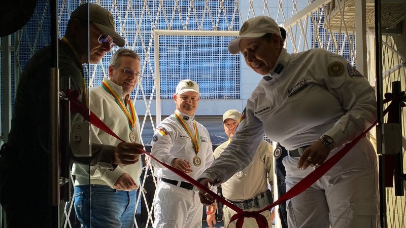 A imagem mostra uma servidora do departamento de sa&uacute;de da Brigada Militar cortando a faixa de reinaugura&ccedil;&atilde;o da Policl&iacute;nica Odontol&oacute;gica Central (POC) do Centro M&eacute;dico-Odontol&oacute;gico da Brigada Militar. Ela veste uma farda branca e segura uma tesoura com a m&atilde;o direita. Ao lado dela, est&aacute; o comandante-geral da Brigada Militar, Cl&aacute;udio dos Santos Feoli. Ao fundo, est&atilde;o outros servidores da Brigada Militar