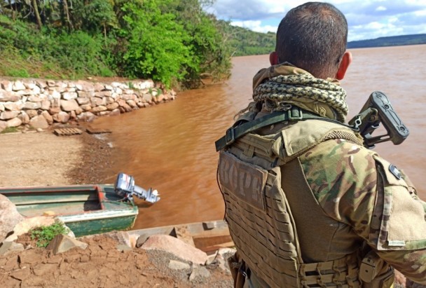 Soldado do Bope fardado observa barco em leito de rio