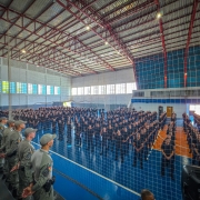 A imagem mostra os novos alunos-soldados em formação no  ginásio da Escola de Educação Física da Brigada Militar, em Porto Alegre. Também é possível observar policiais militares fardados na imagem