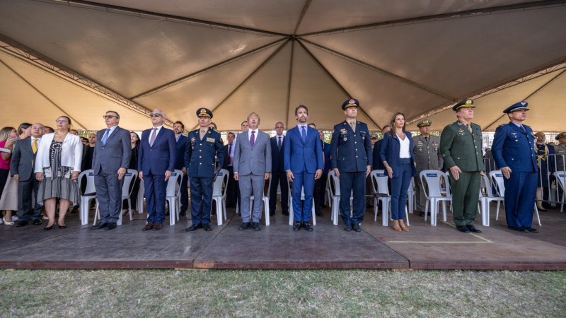 A foto mostra uma fileira de autoridades e integrantes do Corpo de Bombeiros posicionados em p&eacute; sobre um palco elevado. Algumas pessoas vestem uniformes militares escuros ou verdes, enquanto outras usam trajes sociais formais.