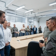 Amplo sagu&atilde;o com v&aacute;rias pessoas, civis e policiais militares. Em primeiro plano, dois homens vestidos de roupas civis conversam com dois homens vestidos de policiais militares, observados por um homem vestido com roupas civis