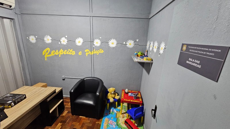 Sala de atendimento identificada como &ldquo;Sala das Margaridas&rdquo;, com decora&ccedil;&atilde;o acolhedora e tem&aacute;tica infantil. O espa&ccedil;o inclui poltrona, mesa de trabalho, brinquedos, tapete colorido e prateleira com objetos. Na parede, h&aacute; o texto &ldquo;Respeito e Prote&ccedil;&atilde;o&rdquo; em amarelo, al&eacute;m de flores decorativas.