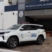 Uma fotografia colorida em plano m&eacute;dio e perspectiva em tr&ecirc;s quartos capta uma viatura oficial de Per&iacute;cia Criminal estacionada em frente &agrave; sede do Instituto-Geral de Per&iacute;cias do Rio Grande do Sul 