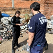 A imagem mostra dois servidores das for&ccedil;as de seguran&ccedil;a do Estado, uma mulher e um homem, analisando um material apreendido durante a opera&ccedil;&atilde;o 